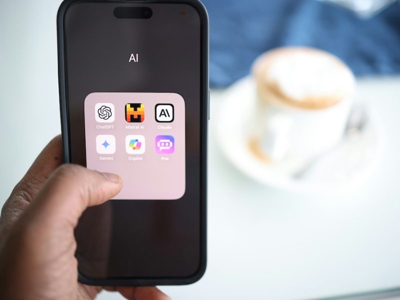 Hand holding a phone showing AI app icons beside a cup of coffee