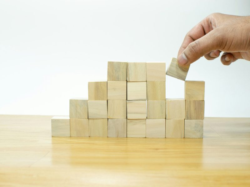 Hand placing a wooden block on top of a stack of blocks