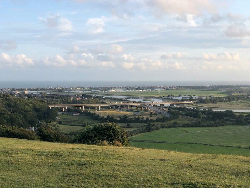 Green hillside overlooking farmland, a road bridge and the coast