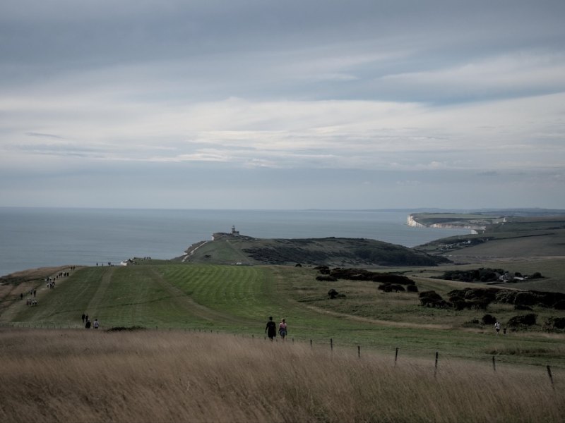 Two walkers on a clifftop path with a lighthouse in the distance