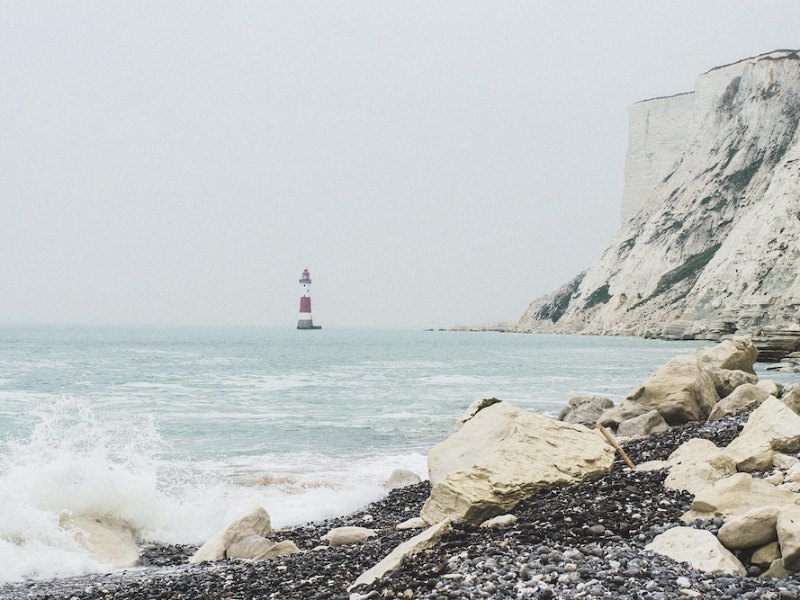 Waves on a rocky beach with chalk cliffs and a striped lighthouse