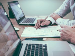 Hand writing notes beside two laptops on a desk