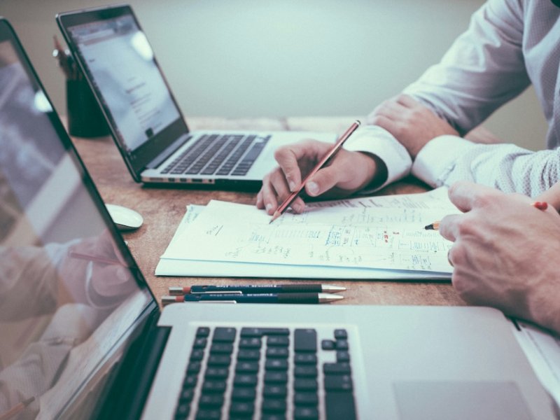 Hand writing notes beside two laptops on a desk