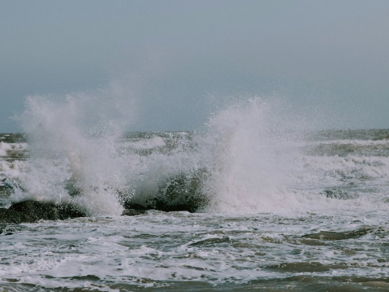 Waves crashing against a sea wall with white cliffs in the distance