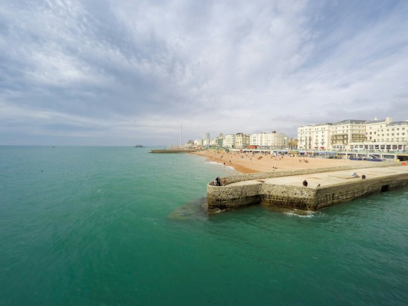 Green sea beside a harbour wall with a seafront town in the distance